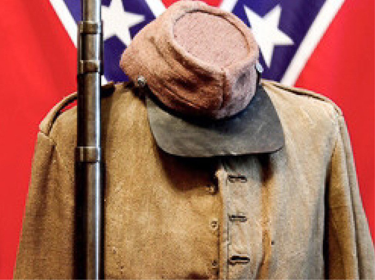 A worn Confederate uniform and cap sit on a headless mannequin before a Confederate flag, with an upright rifle positioned nearby.